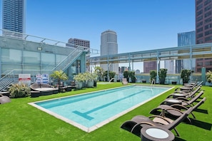 Ein Pool auf dem Dach mit Glasveranda, Liegestühlen und Blick auf die Stadt.