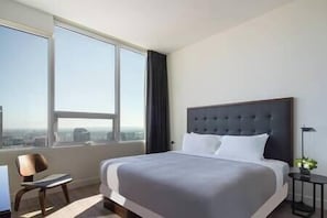 A hotel room with a large bed, a chair, a small table, and a view of the city through large windows. - Highrise 2b 2b Apartment Conv Center-Heart Of Downtown LA (Los Angeles)