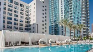 Ein Pool mit Liegestühlen und Sonnenschirmen, umgeben von hohen Gebäuden.