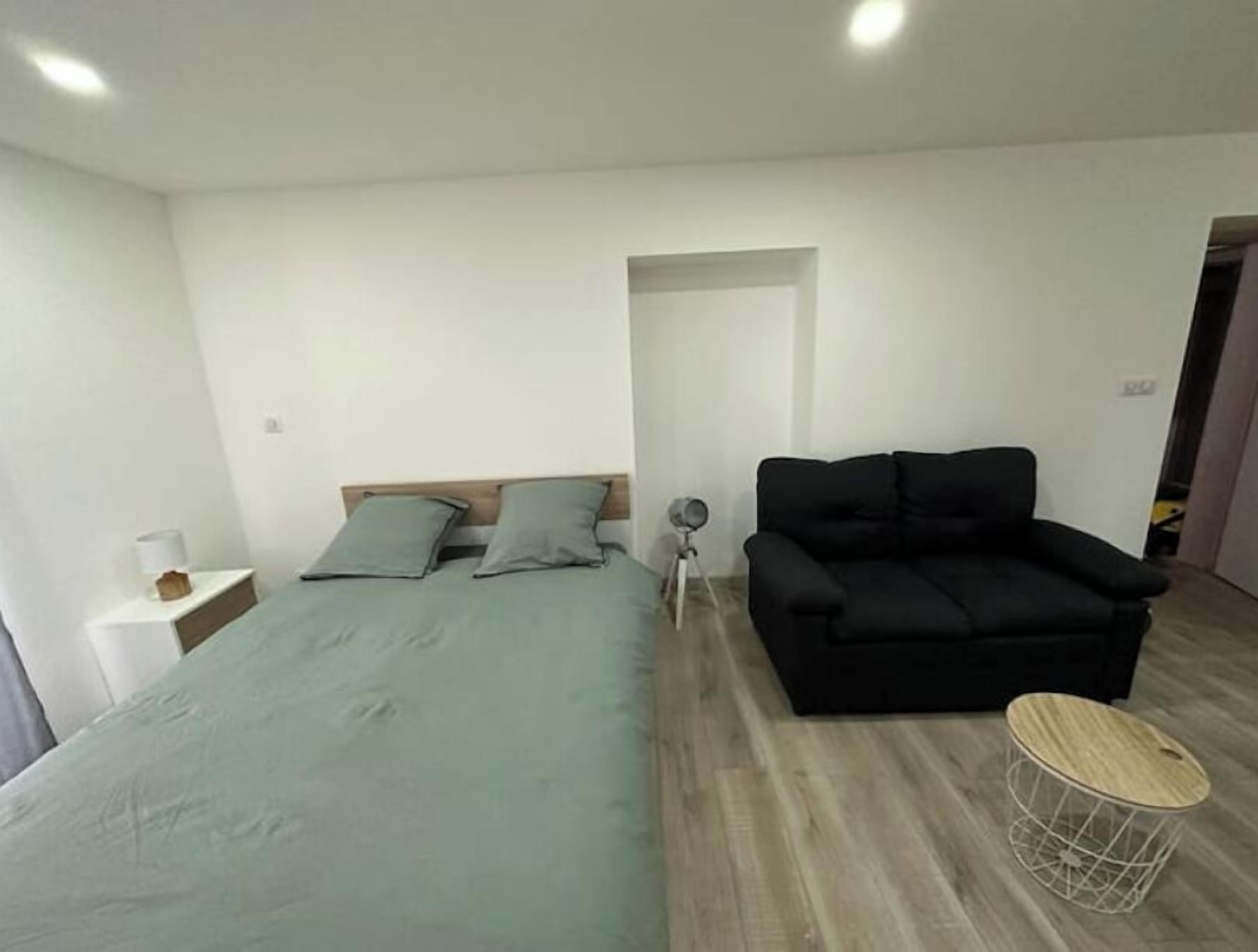 Une chambre moderne avec un lit, un canapé noir, une petite table ronde et une lampe.