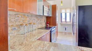 A kitchen with granite countertops, wooden cabinets, a brick backsplash, and stainless steel appliances.