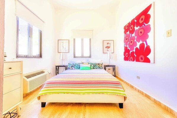 A bedroom with a large bed, a dresser, a radiator, and a wall with a red floral pattern.