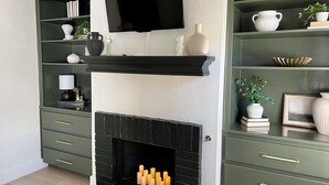 Uma sala de estar moderna com lareira, televisão na parede e estante com objetos decorativos.