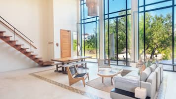 Amplia sala de estar con una escalera de madera, ventanas grandes, un sofá y una mesa de comedor.