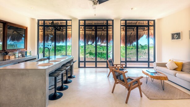 A modern kitchen with a bar area, large windows, and a ceiling fan. - Casa Imox (Isla Holbox)