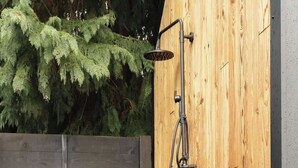 Eine hölzerne Dusche im Freien mit einem Metall-Brausekopf, einer kleinen Pflanze und einem Holzboden.