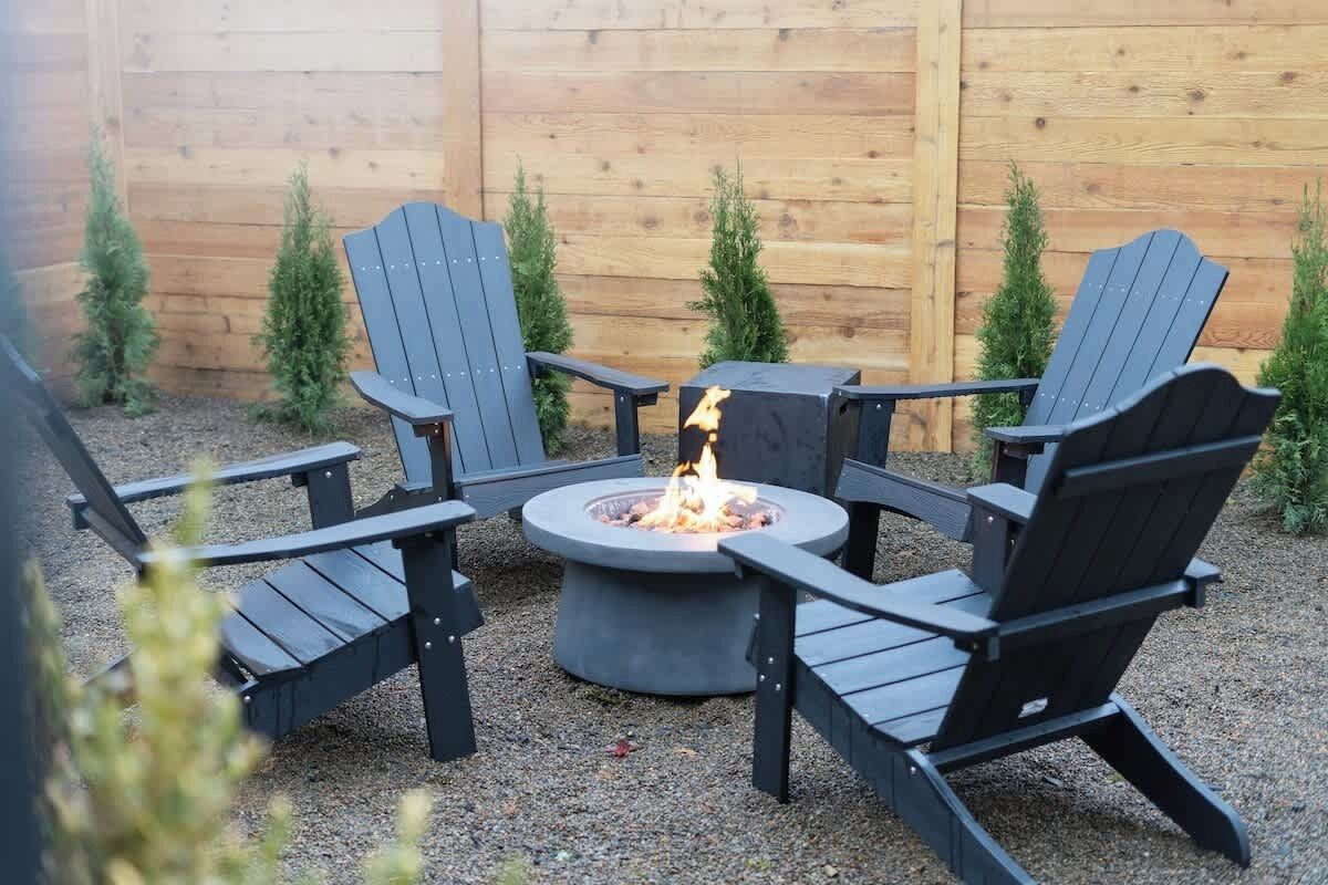 Een vuurkuil omringd door vier Adirondack-stoelen in een tuin.