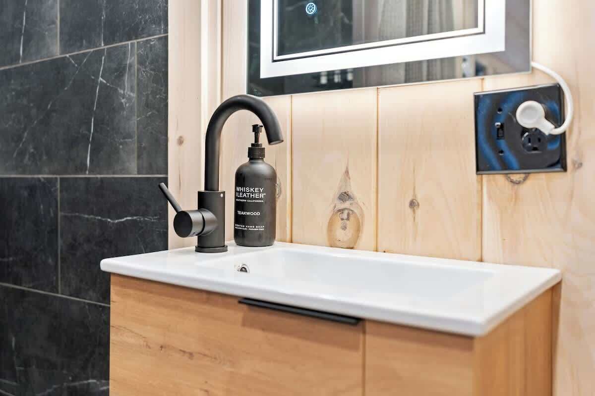 A bathroom with a modern sink, a black faucet, and a bottle of whiskey leather soap.