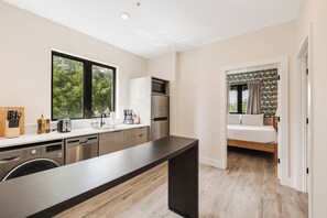A modern kitchen with a dishwasher, a built-in oven, and a microwave. There is a large window providing a view of greenery outside. - Roami at The Palace (Miami)