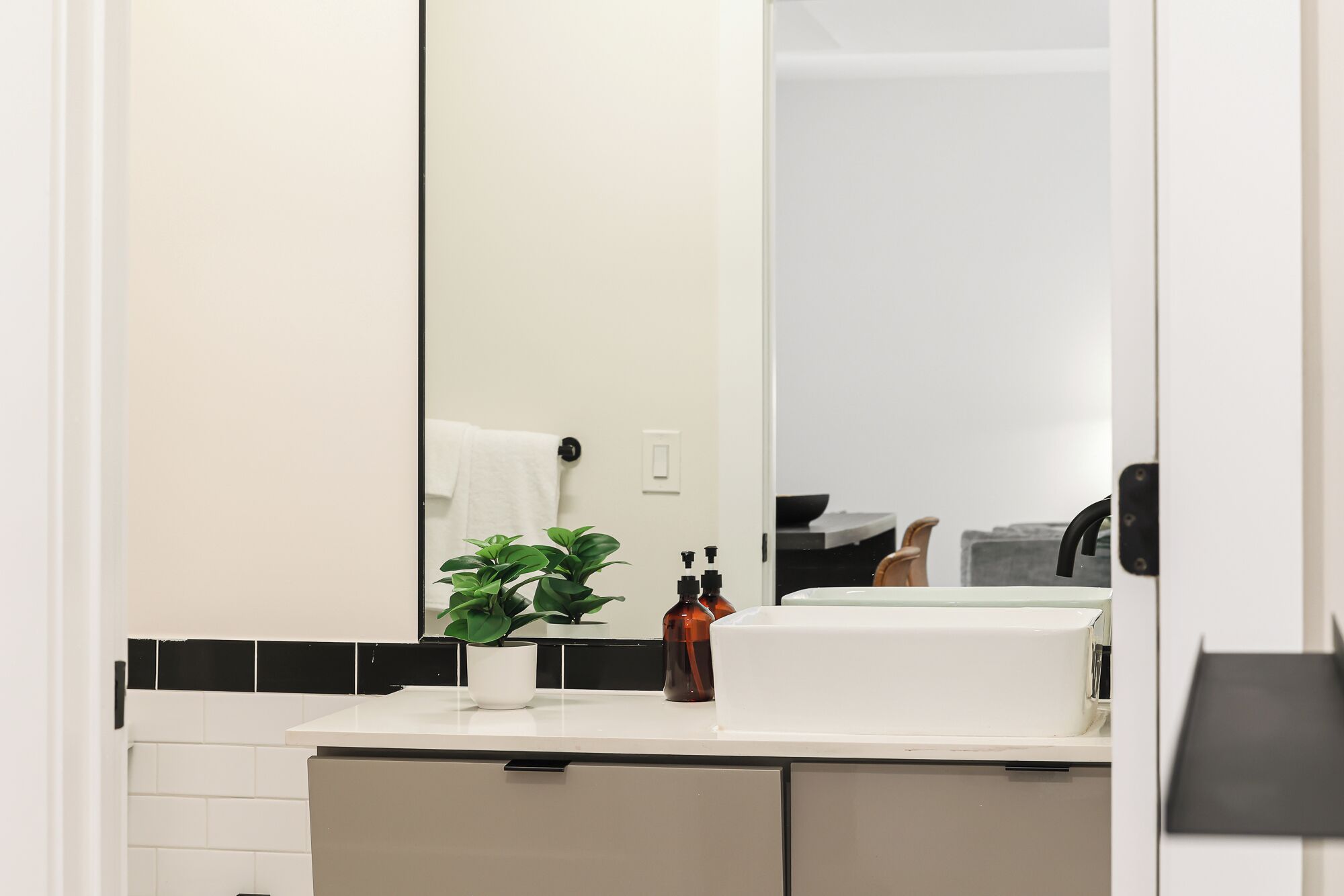 A bathroom with a white sink, a mirror, a potted plant, and a towel hanging on a towel rack.
