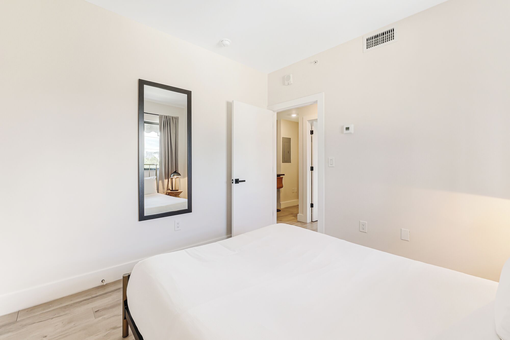 A bedroom with a large bed, a mirror, and a door leading to another room.