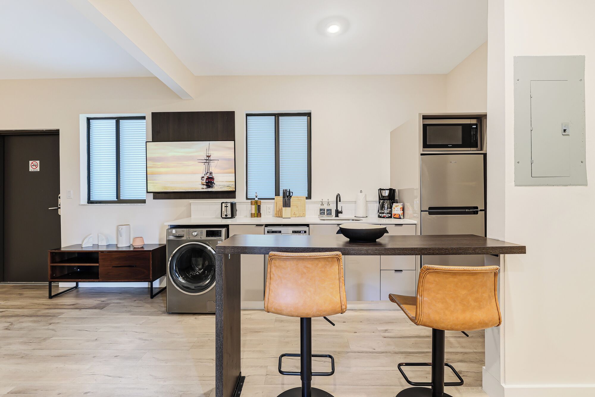 A modern kitchen with a central island, a washing machine, and two bar stools.