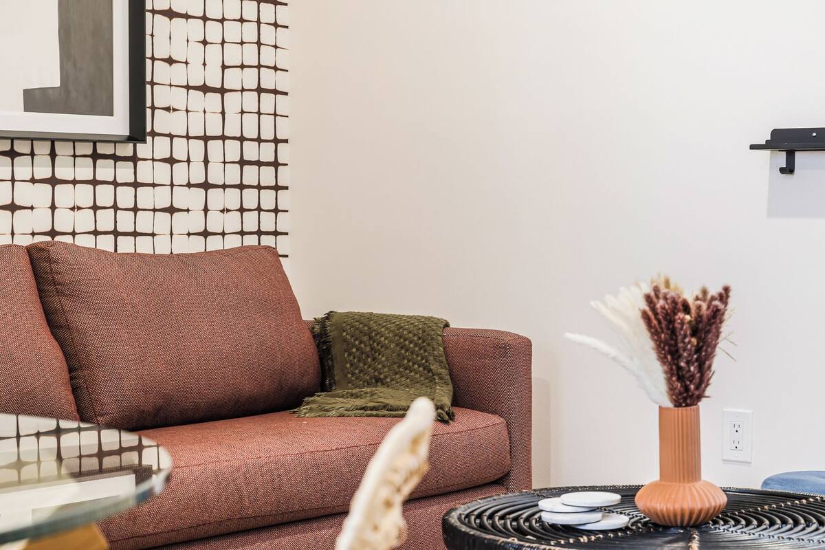 Una sala de estar con una pared estampada, un sofá, una mesita con un jarrón y una estantería de pared.