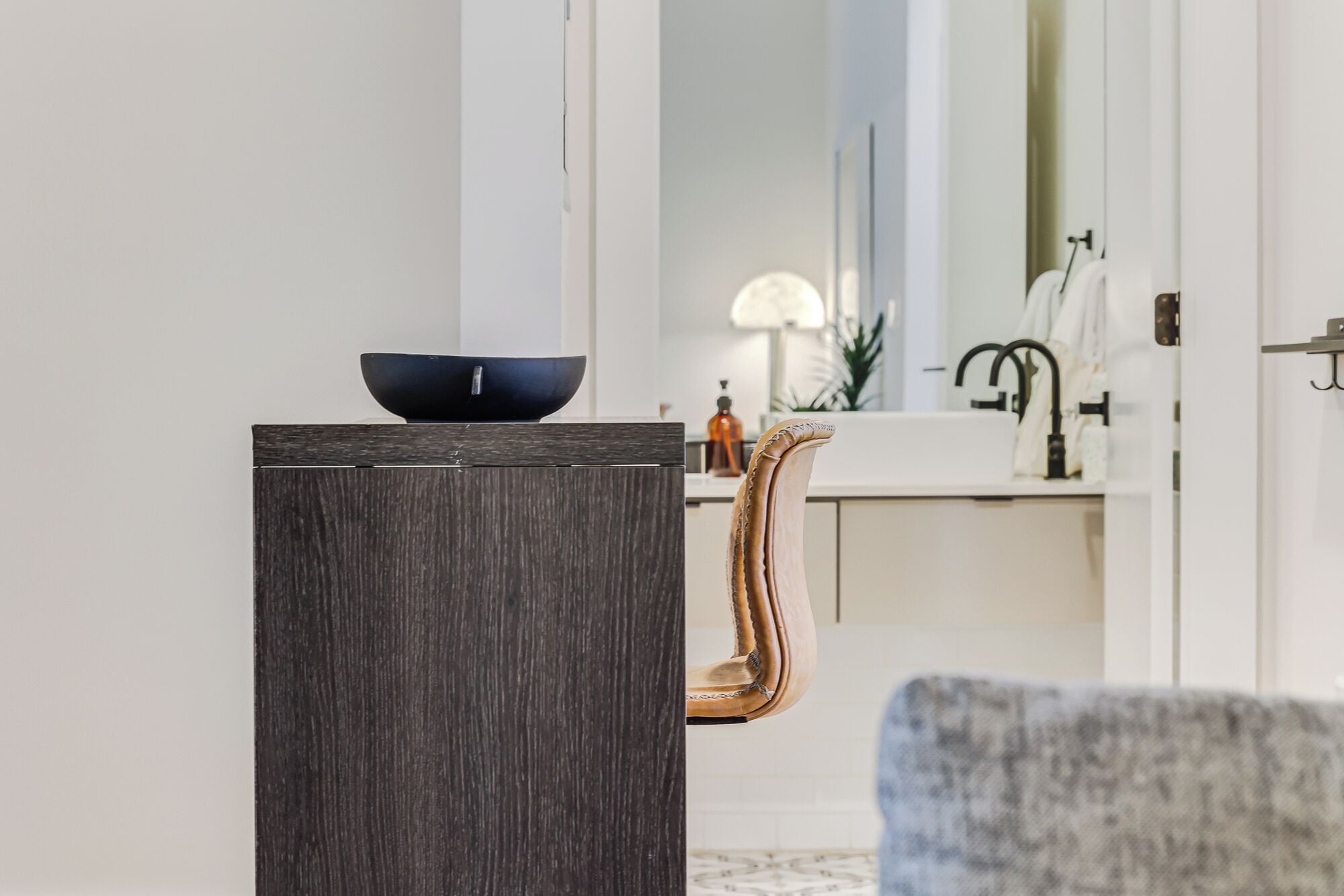 Ein modernes Badezimmer mit einem dunklen Holz-Waschtisch, einer schwarzen Schale darauf und einem weißen Waschbecken mit schwarzem Wasserhahn.