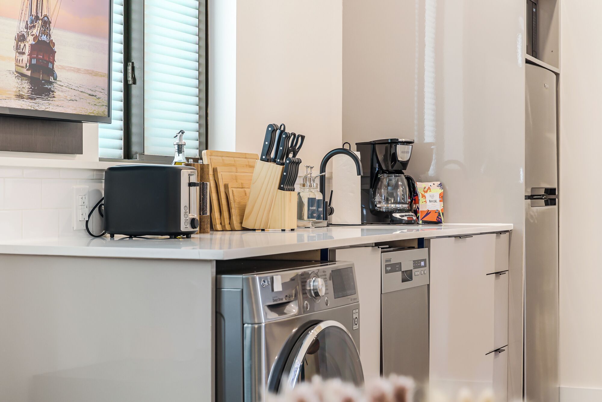 A compact kitchen with a toaster, coffee maker, and a washing machine.