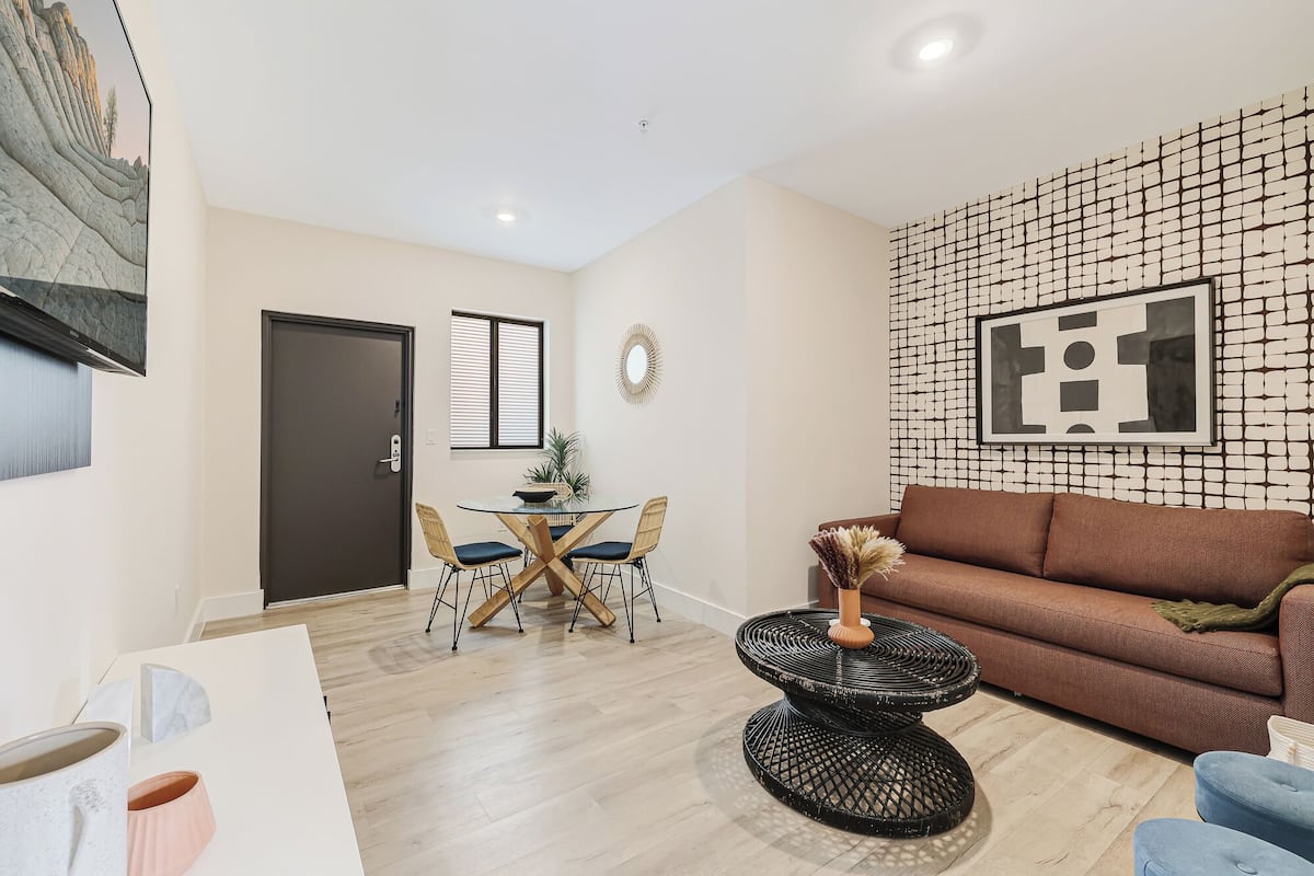 Una sala de estar moderna con un sofá marrón, una mesa de centro redonda negra y un comedor con mesa de vidrio y sillas de mimbre.