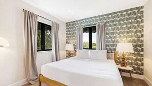 Une chambre d’hôtel avec un grand lit, deux fenêtres avec des rideaux, un mur à motifs et deux lampes de chevet.
