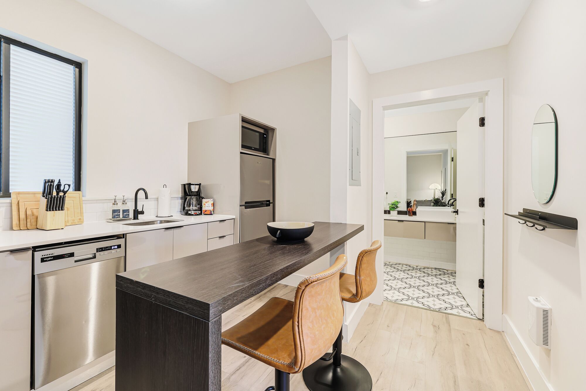 A modern kitchen with a dishwasher, a coffee maker, and a bowl on the counter. There are two chairs and a small table.