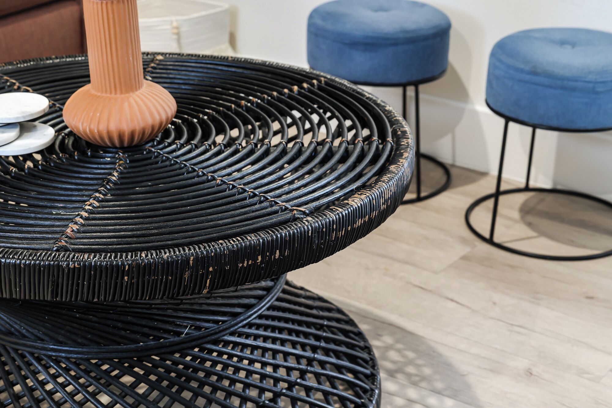 Une chaise en osier dotée d’un siège et d’un dossier texturés, accompagnée de deux poufs bleus et d’une petite table ronde.