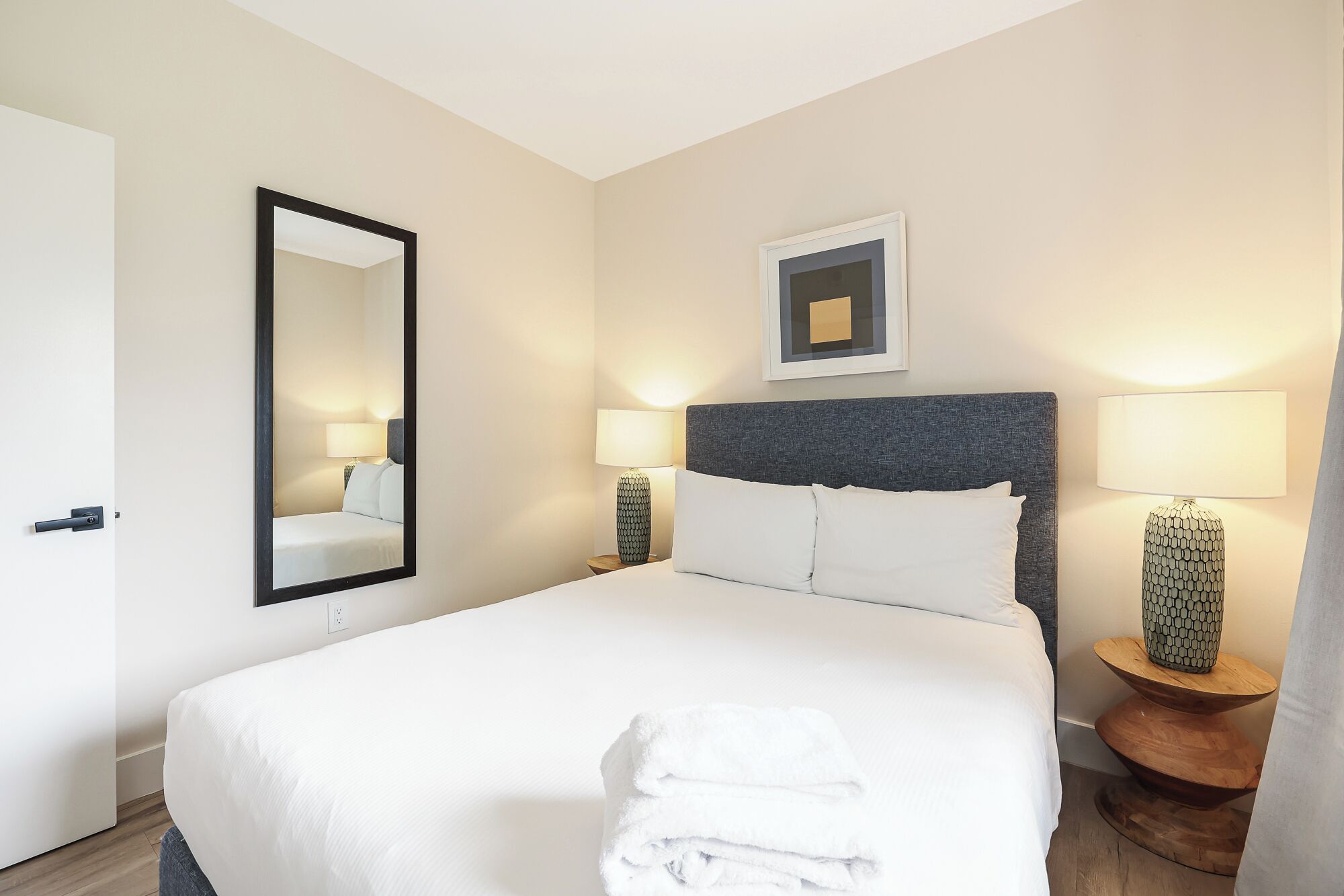 A hotel room with a large bed, two bedside tables with lamps, a mirror, and a framed picture on the wall.