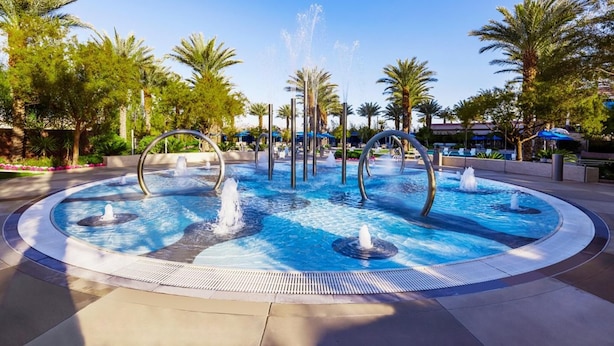 A circular pool with multiple fountains and palm trees around it. - 1Bed/1Bath Desert Blue Margaritaville! (Las Vegas)