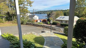A residential area with a stone pathway leading to a driveway, surrounded by greenery and houses with a view of a lake.