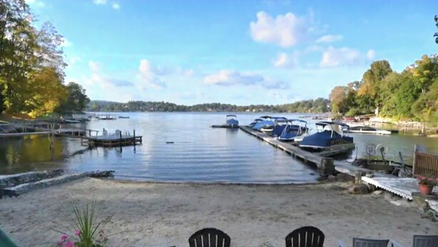 A lakeside view with docked boats, a sandy beach, and chairs.