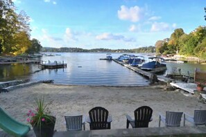 A lakeside view with docked boats, a sandy beach, and chairs. - 3-bedroom Candlewood Lakeside house (Danbury)