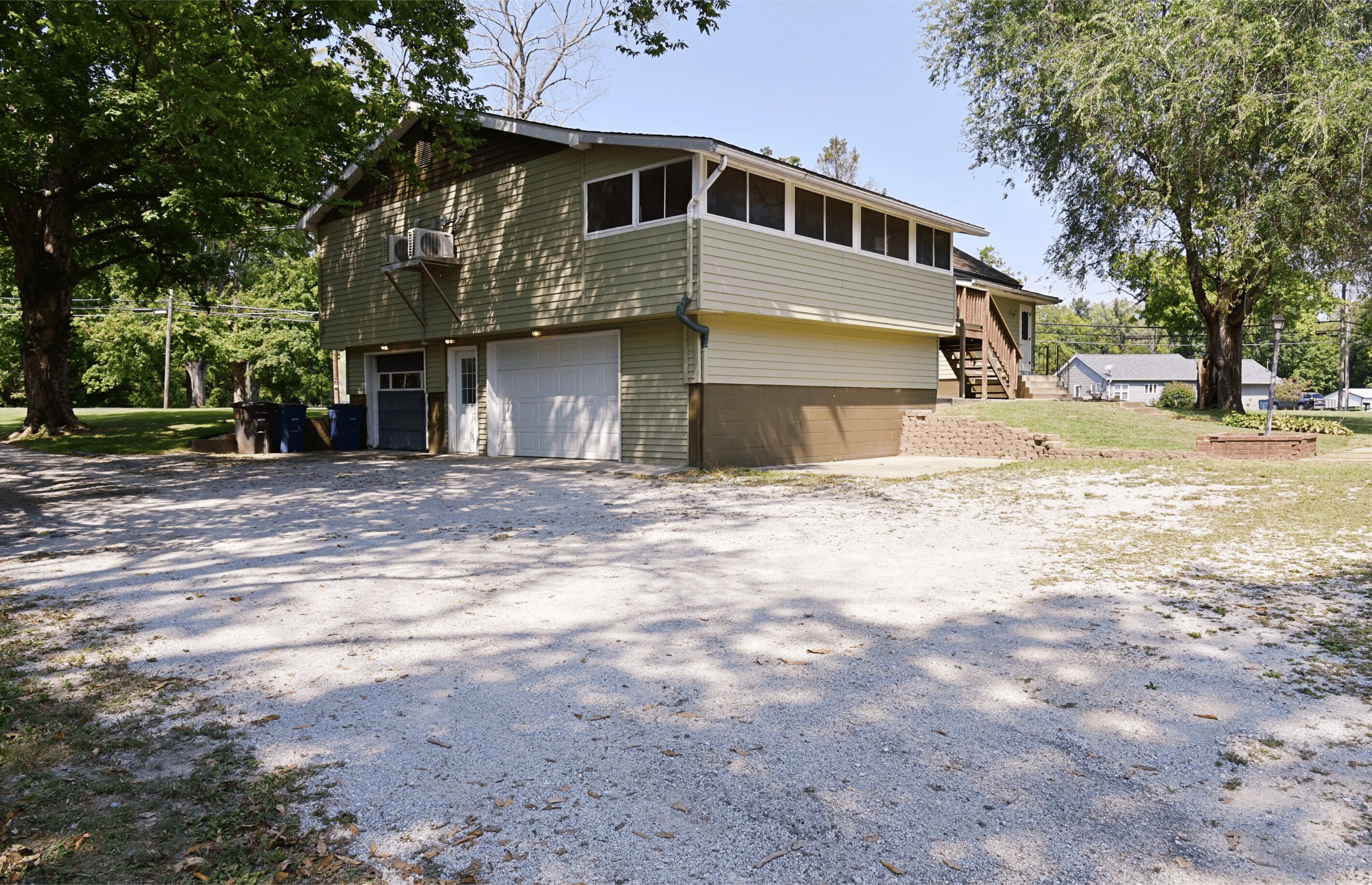 Ein zweigeschossiges Haus mit Garage, überdachter Veranda und einem Schotterweg.
