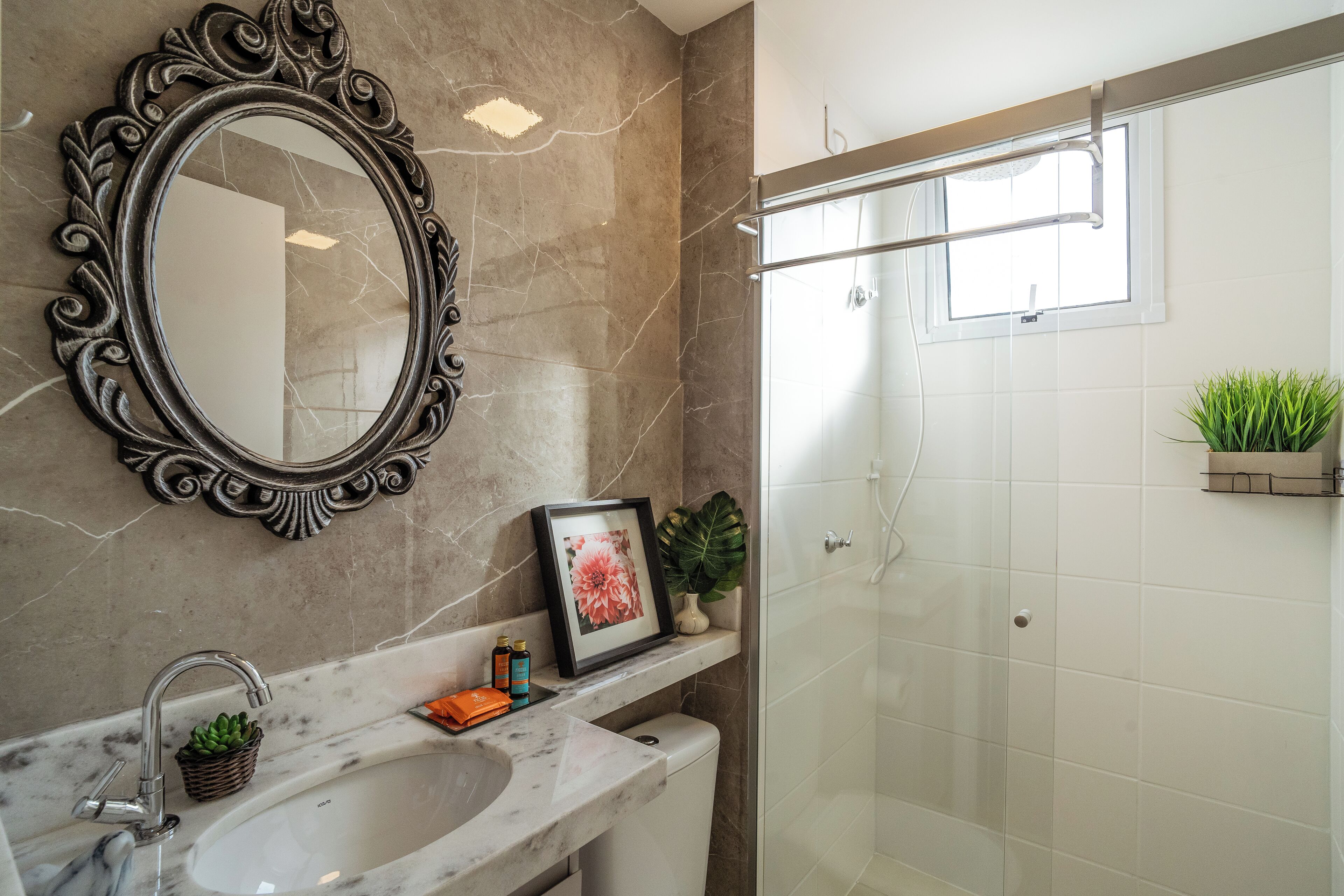 A bathroom with a marble sink, a framed picture, a small plant, and a shower with a window.