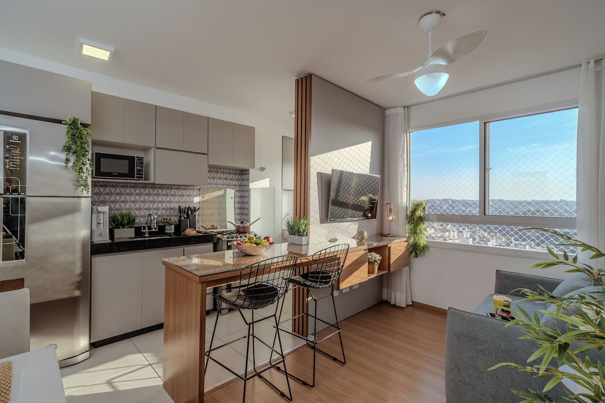 Cozinha moderna com ilha central, banquetas de bar e uma grande janela com vista para a cidade.