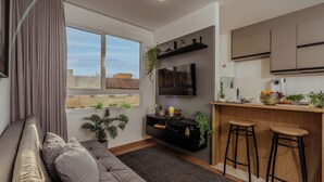 A modern living room with a sofa, a TV, and a kitchen area with bar stools. - Arena MRV, 2 quartos,vaga | Brazilian Corner (Belo Horizonte)