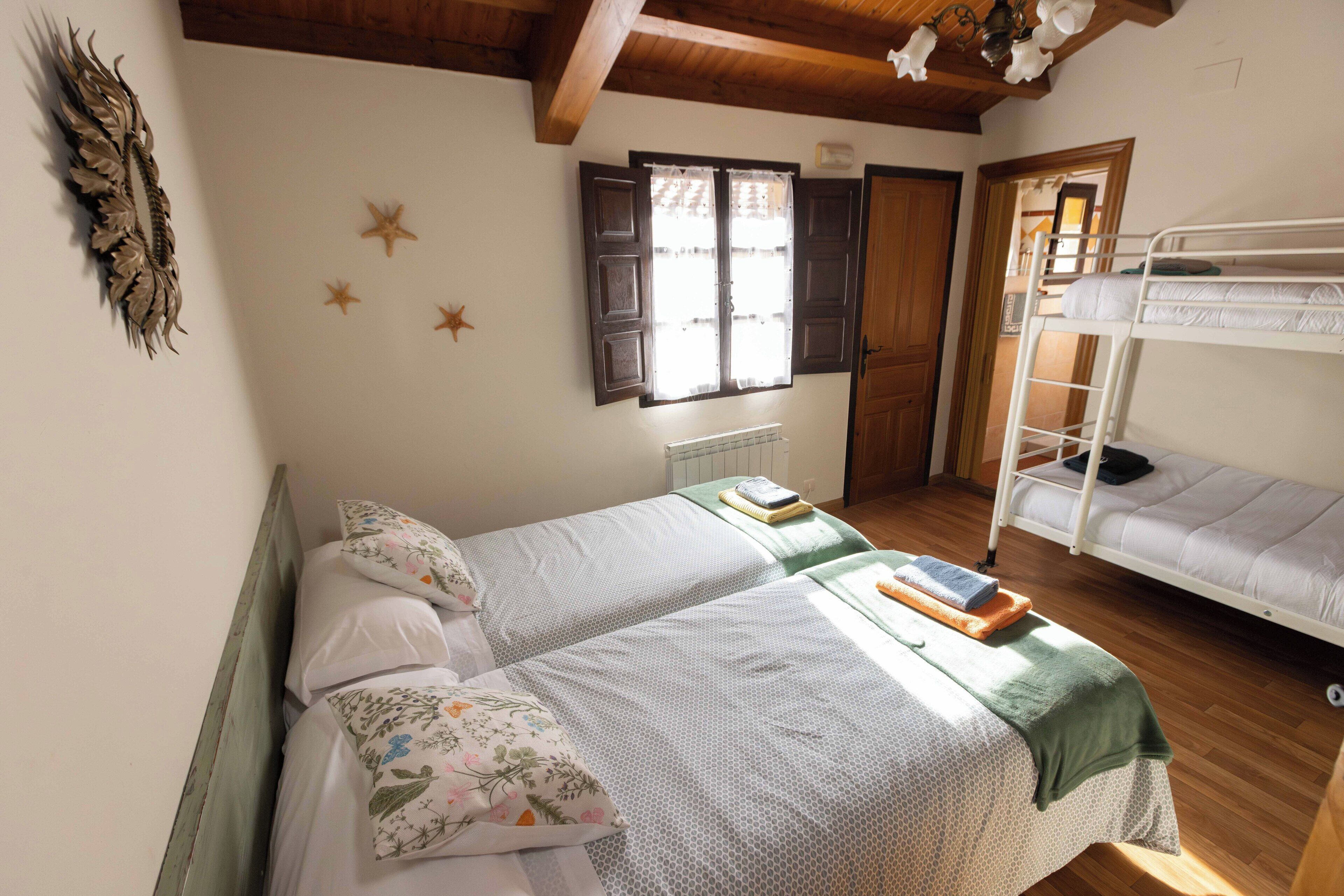 A room with two single beds, a bunk bed, wooden ceiling beams, a window with shutters, and a starfish decoration on the wall.