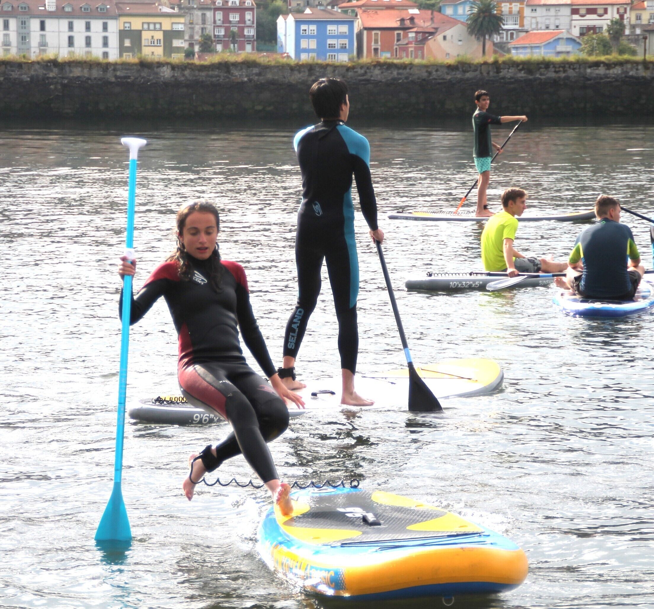 People on paddleboards in a body of water with buildings in the background.