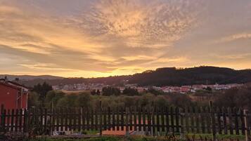 A rural landscape with a wooden fence, a small building, and a distant town under a sunset sky.