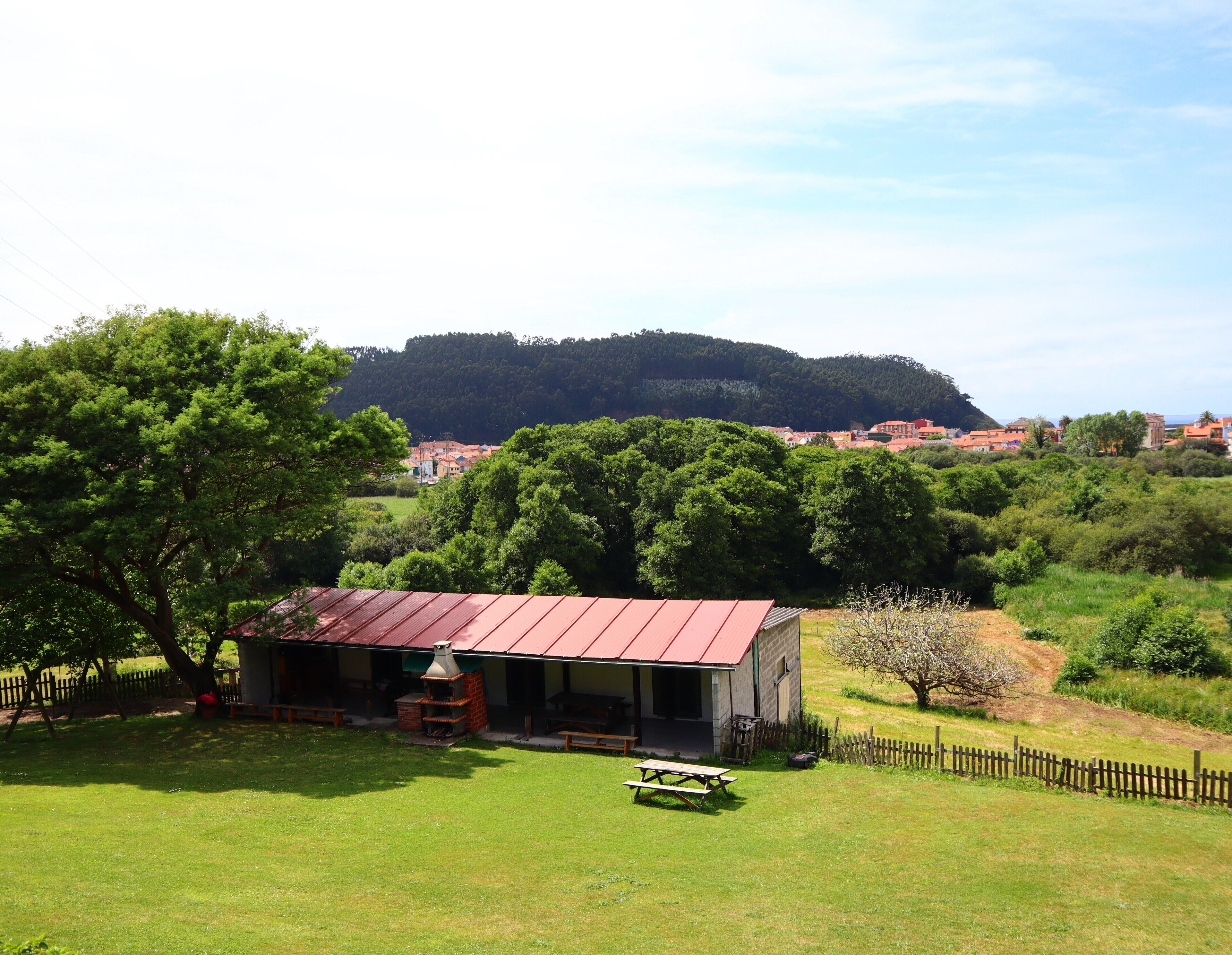 A rustic cabin with a red roof, surrounded by lush greenery and a picnic table in the foreground.