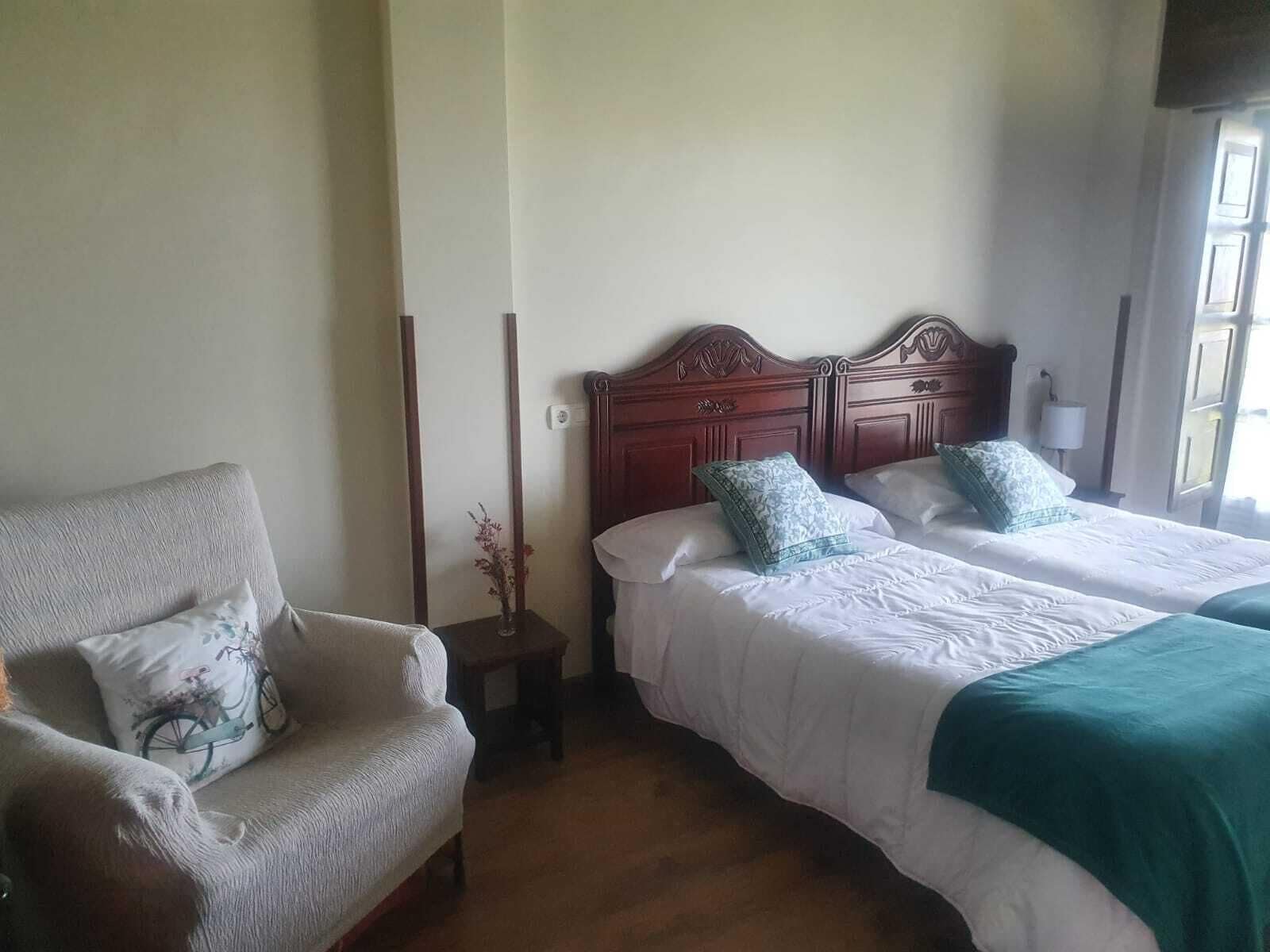 Quarto de hotel com duas camas, uma cadeira e uma pequena mesa com um vaso.
