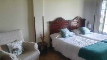 Quarto de hotel com duas camas, uma cadeira e uma pequena mesa com um vaso.