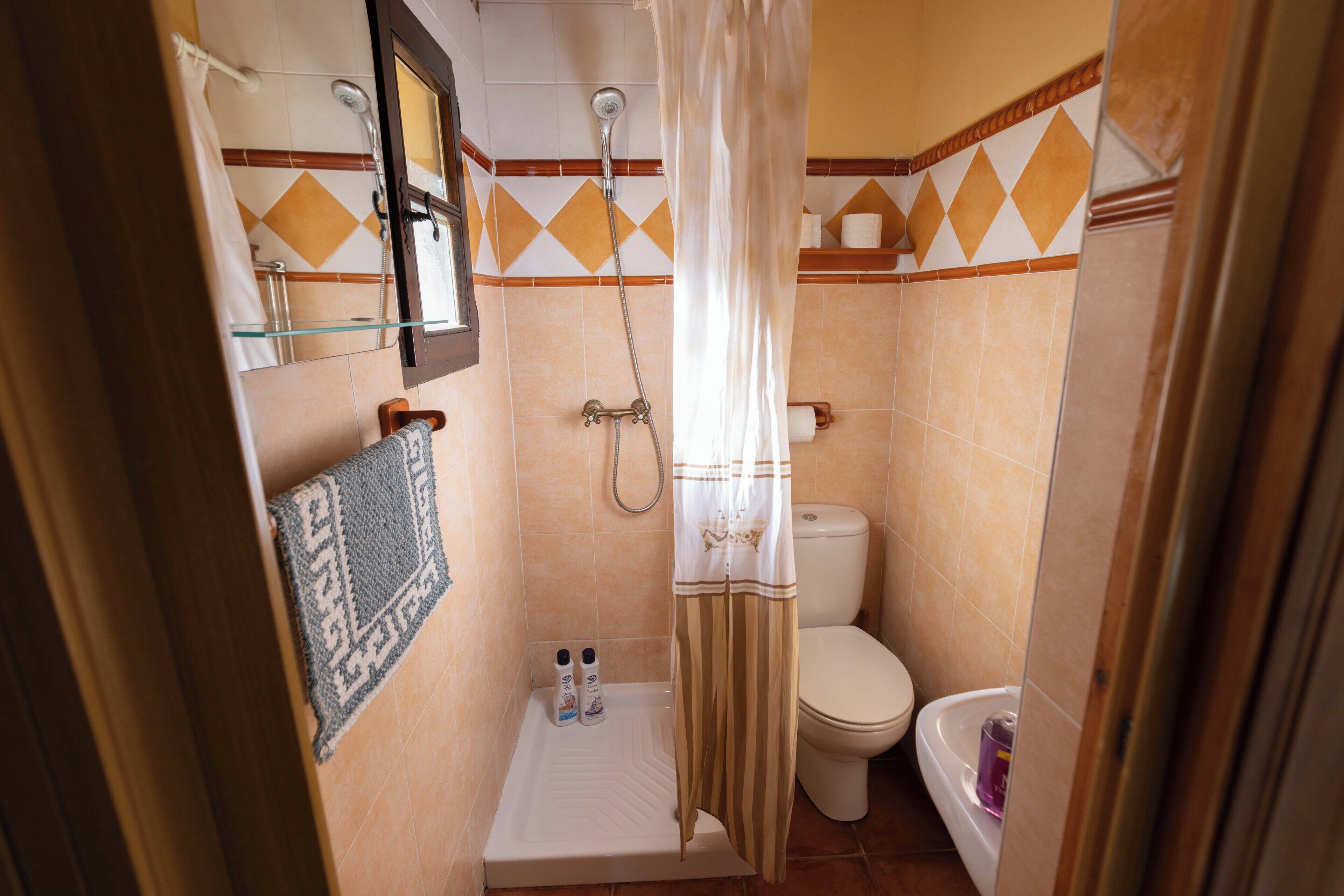 Un baño pequeño con ducha, inodoro y una estantería con artículos de aseo.