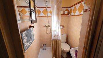 Un baño pequeño con ducha, inodoro y una estantería con artículos de aseo.