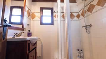 A bathroom with a sink, mirror, window, shower, and toiletries.