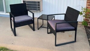 En inglasad uteplats med två fåtöljer i rotting och ett litet bord, en skjutdörr i glas och ett fönster med persienner.