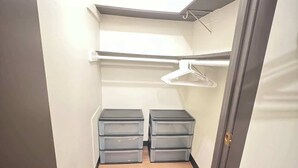 En smal hall med trägolv, ett skåp med två grå förvaringslådor och en klädstång.