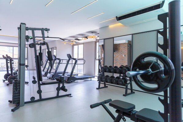 Et fitnessrum med forskellig træningsudstyr, herunder løbebånd, håndvægte og styrkemaskiner.