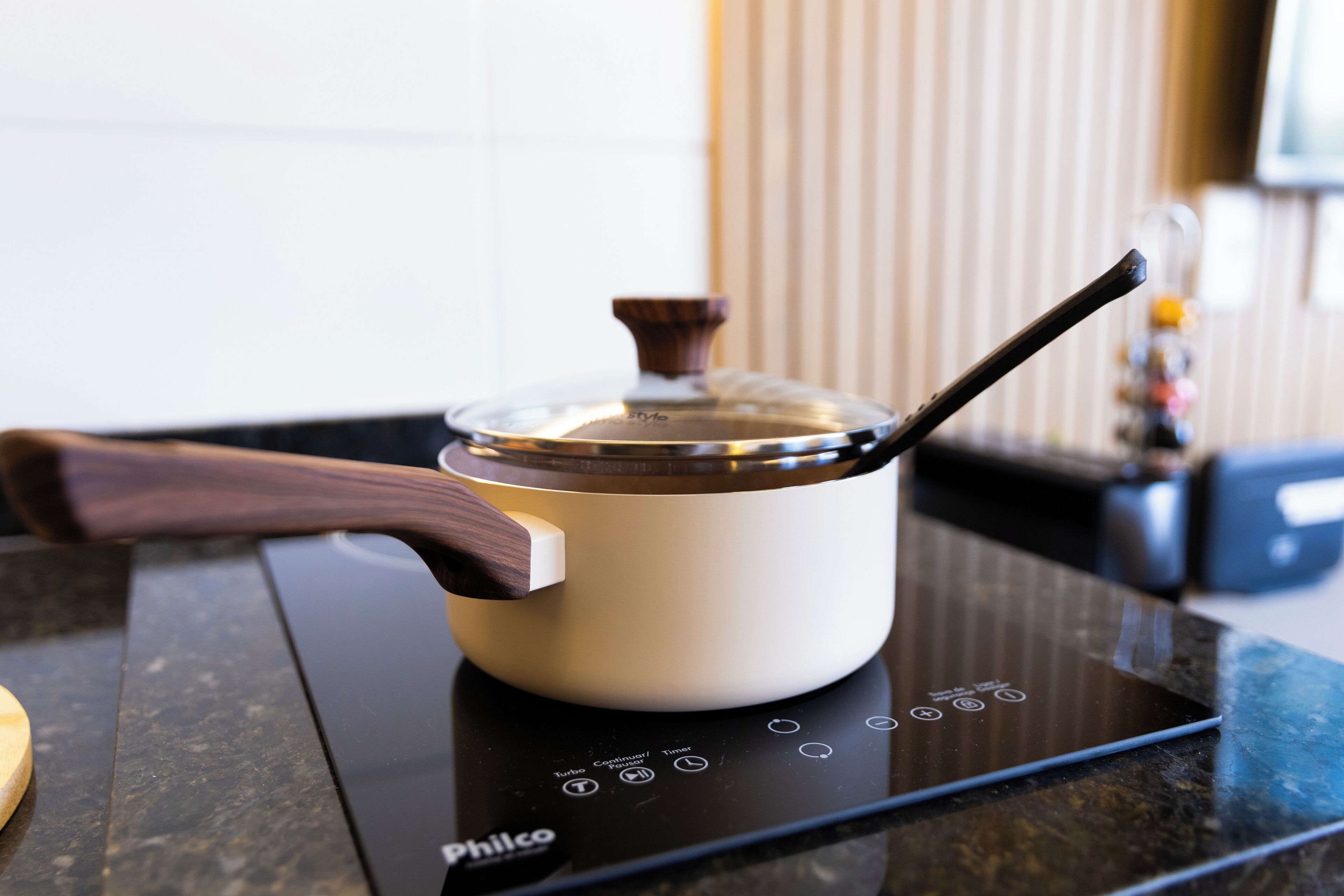A kitchen with a white pot on an induction cooktop, a wooden handle, and a control panel with various settings.