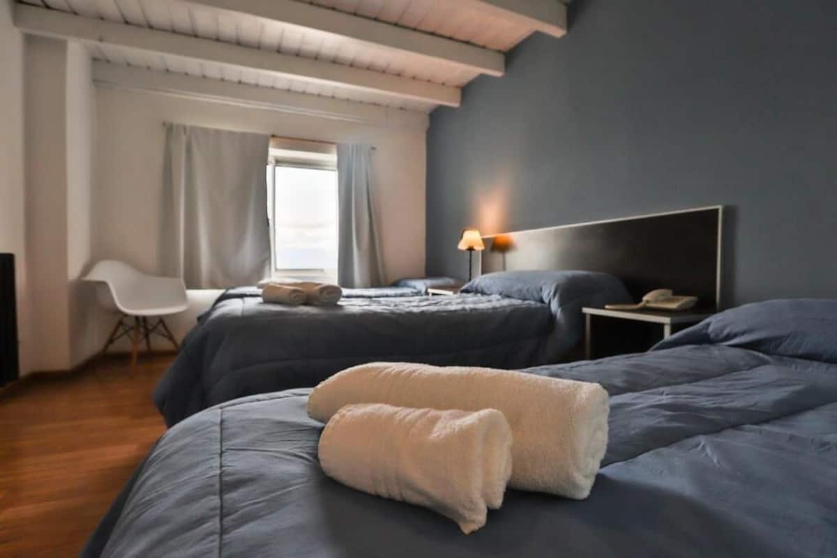 A hotel room with two beds, a desk, a chair, and a window with curtains.
