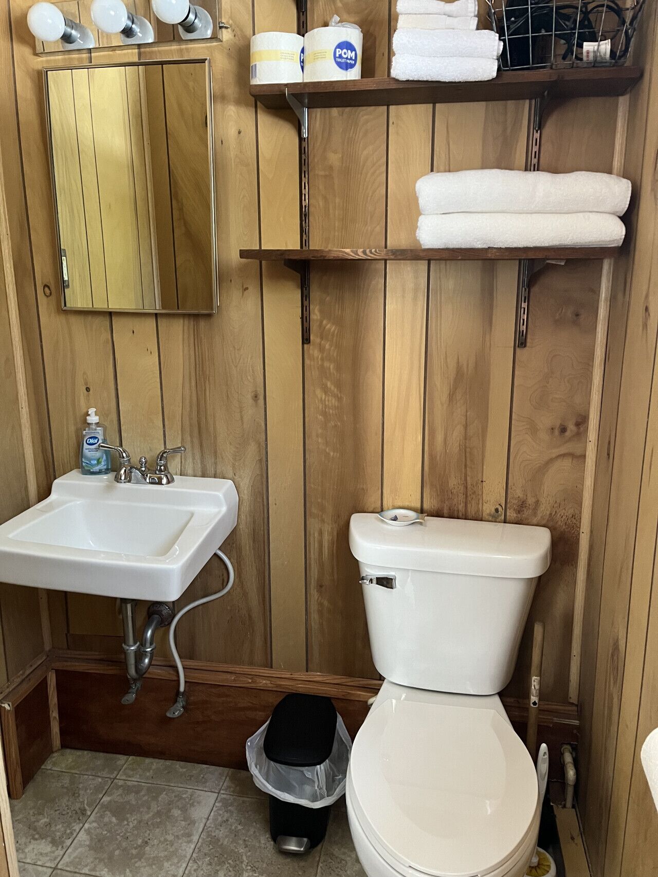 Ein Badezimmer mit Holzwandverkleidung, einem weißen Waschbecken, einer Toilette und einem Mülleimer.