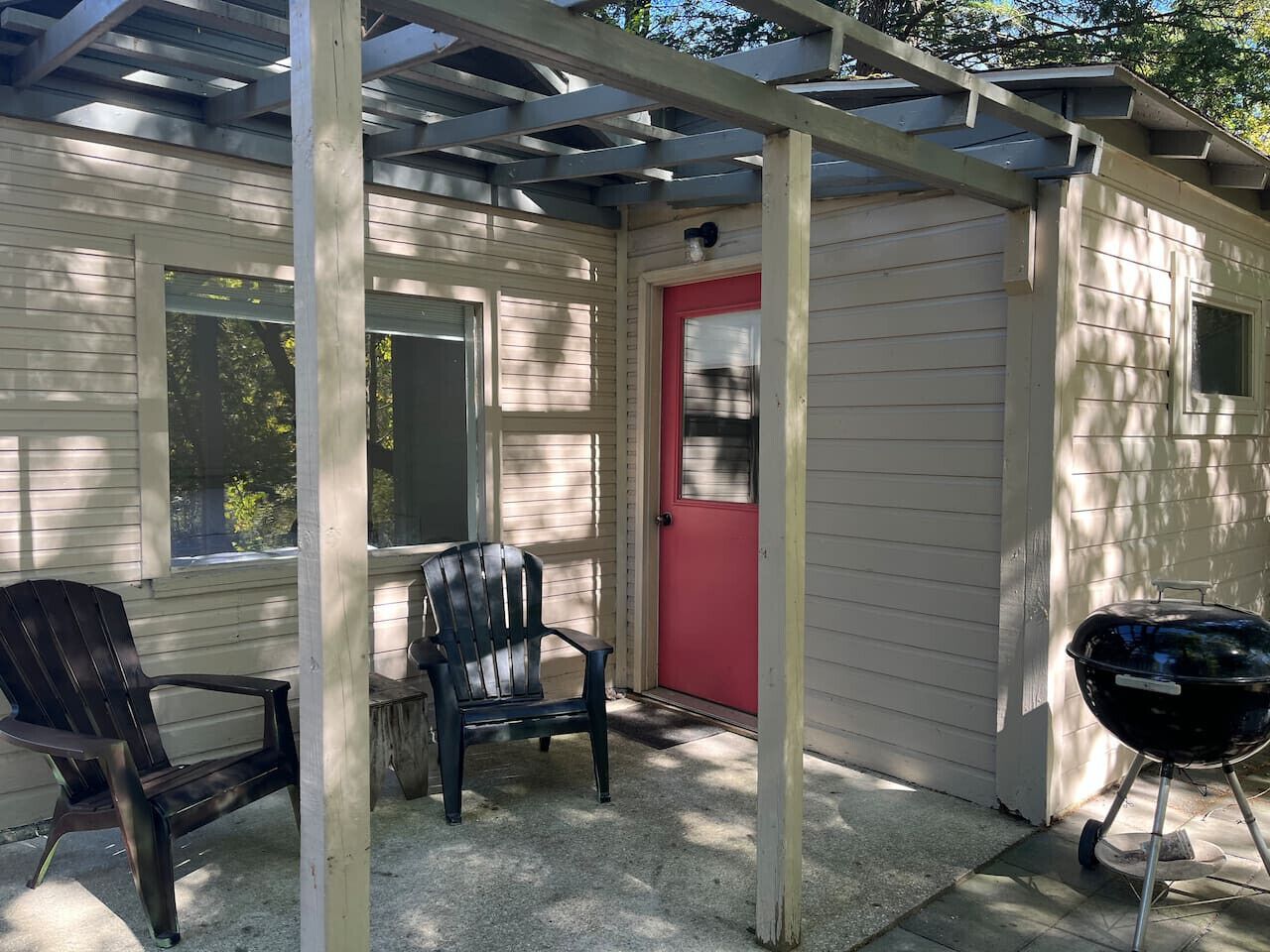 A covered porch with two Adirondack chairs, a red door, and a barbecue grill.