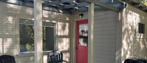 A covered porch with two Adirondack chairs, a red door, and a barbecue grill.