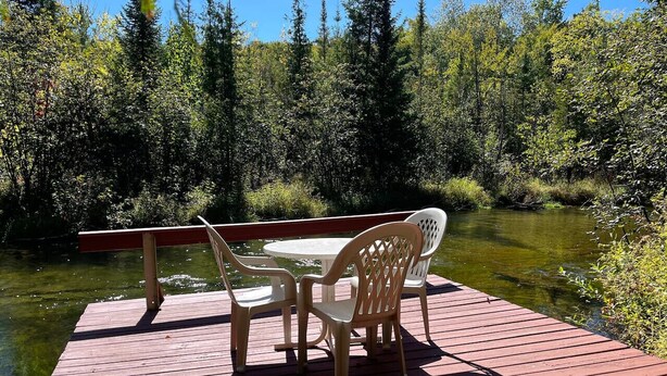 Terraza de madera con una mesa y sillas, con vista al río.